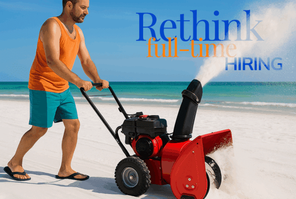 A Florida-man uses a snow-blower on a white-sand beach with the ocean in the background.