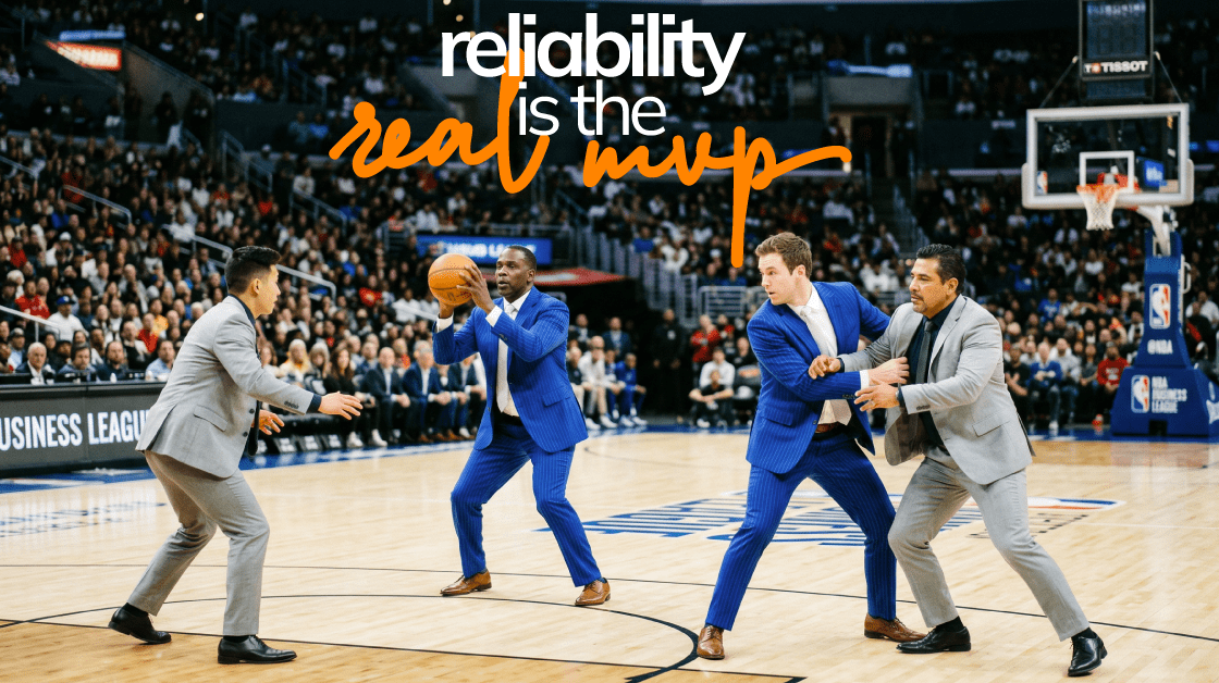 Four men in business suits play basketball in a stadium filled with spectators. Two men wear gray suits, two men wear blue. One player is shown assisting the other depicting reliability in the workplace.